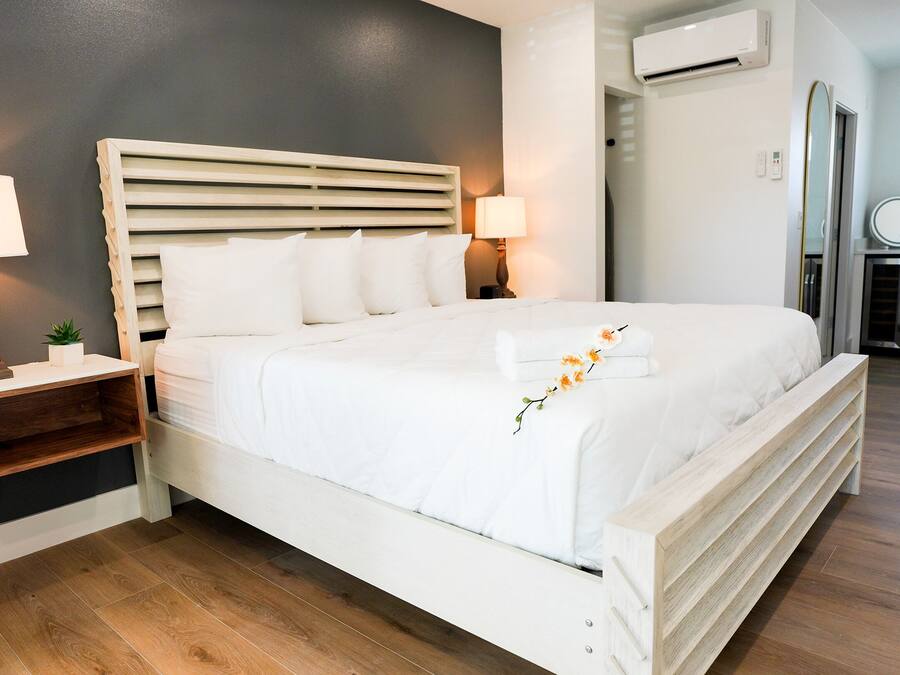 Una camera da letto ordinata con un letto grande, due comodini con lampade, una piccola pianta e un condizionatore d'aria a parete.