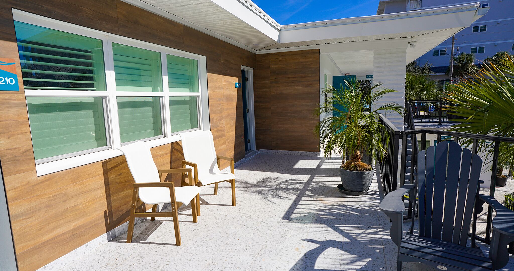 A modern building with a wooden facade, a covered outdoor seating area with chairs, and a potted plant.