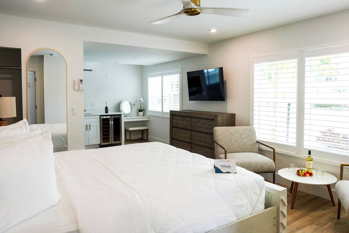 Quarto de hotel com cama, escrivaninha, cadeira, televisão e janela com persianas.