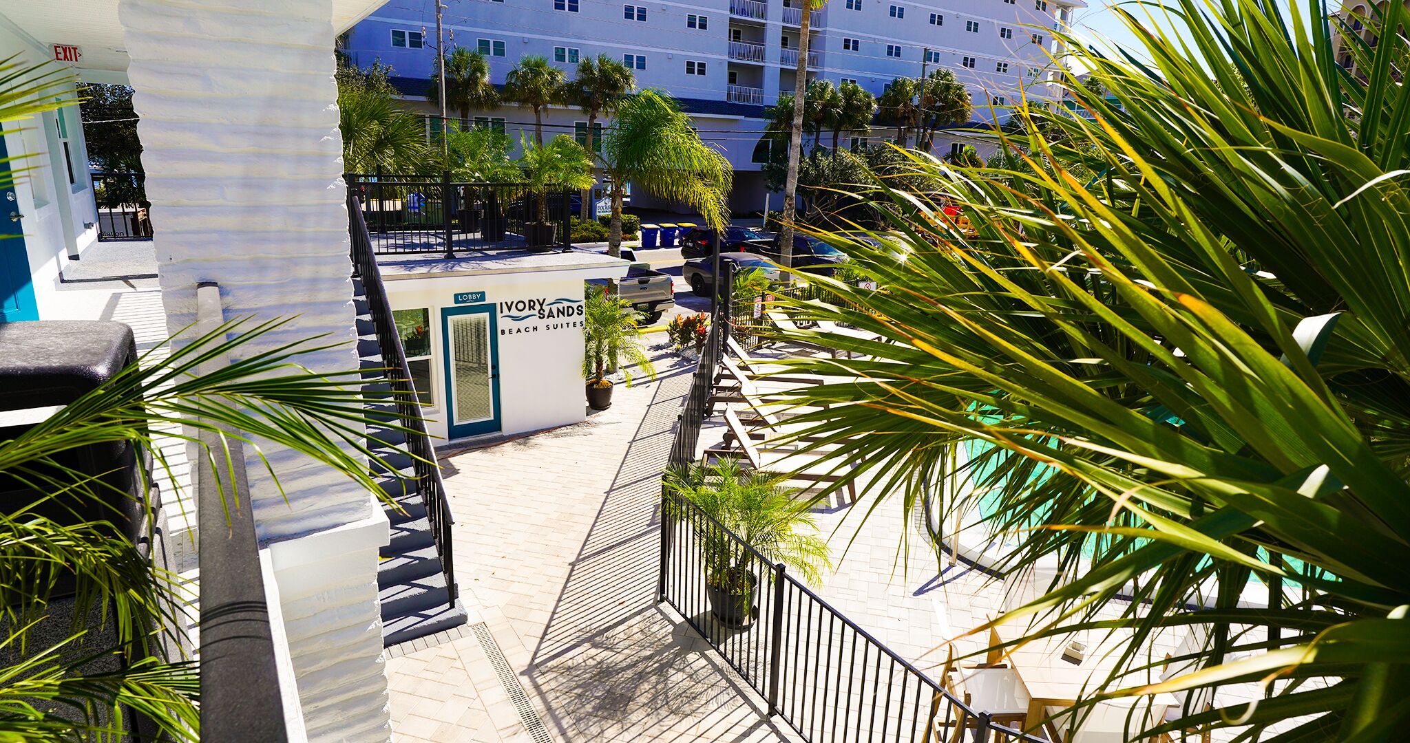 A hotel lobby with a staircase leading to the upper floors, surrounded by palm trees and a pool area.
