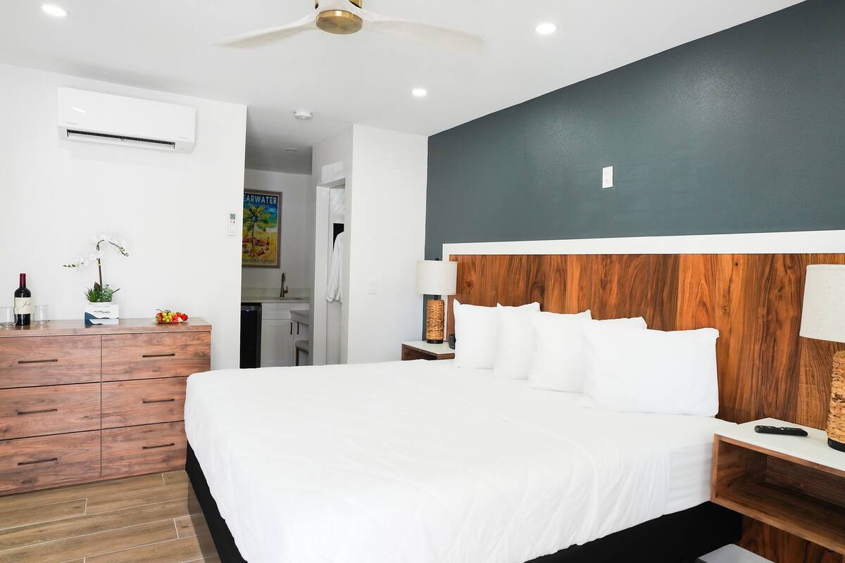 Quarto de hotel moderno com uma cama grande, mesas de cabeceira de madeira, cômoda e ventilador de teto.