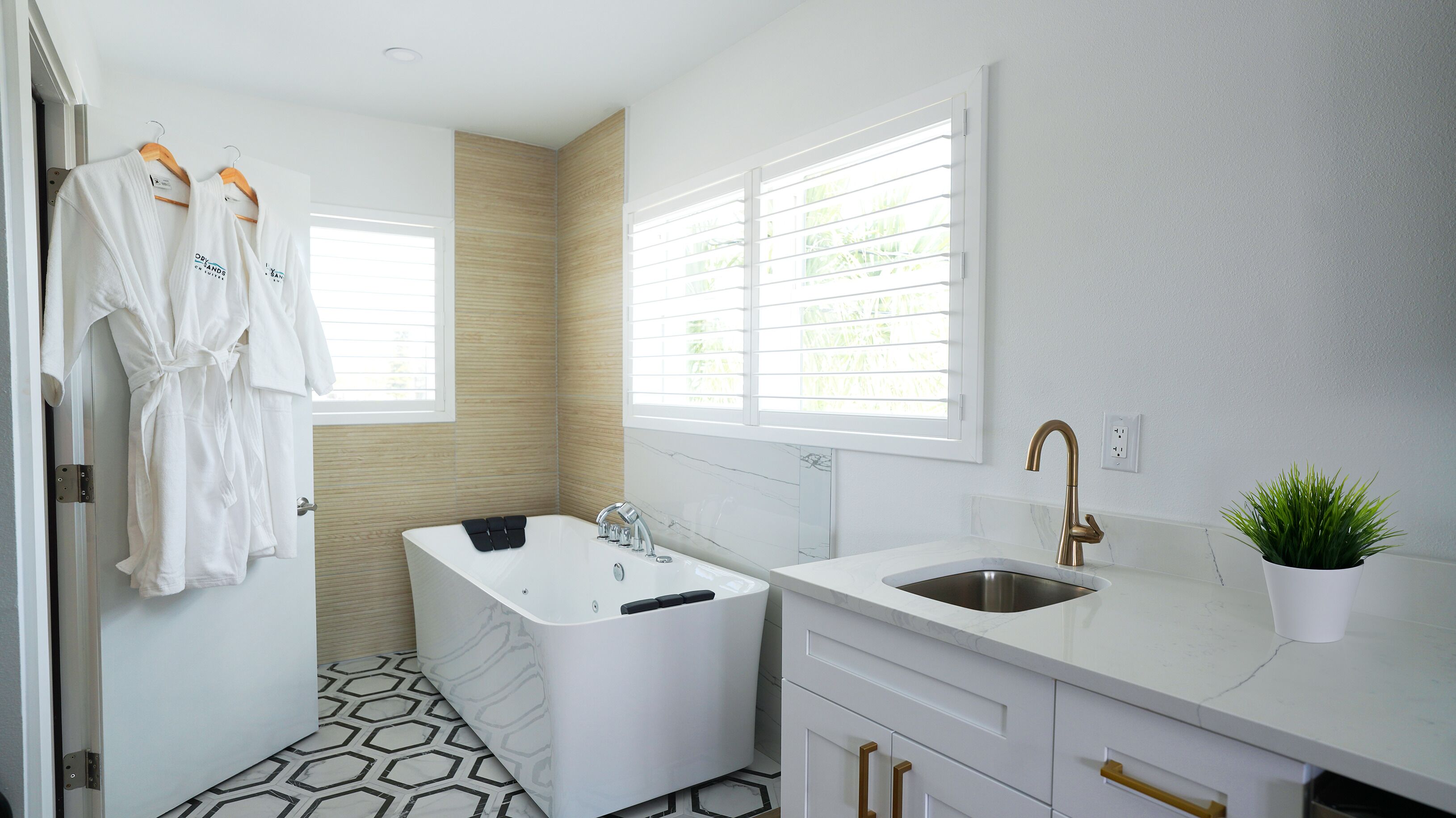 A modern bathroom with a bathtub, a sink, and a window with blinds.