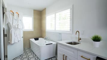A modern bathroom with a bathtub, a sink, and a window with blinds.