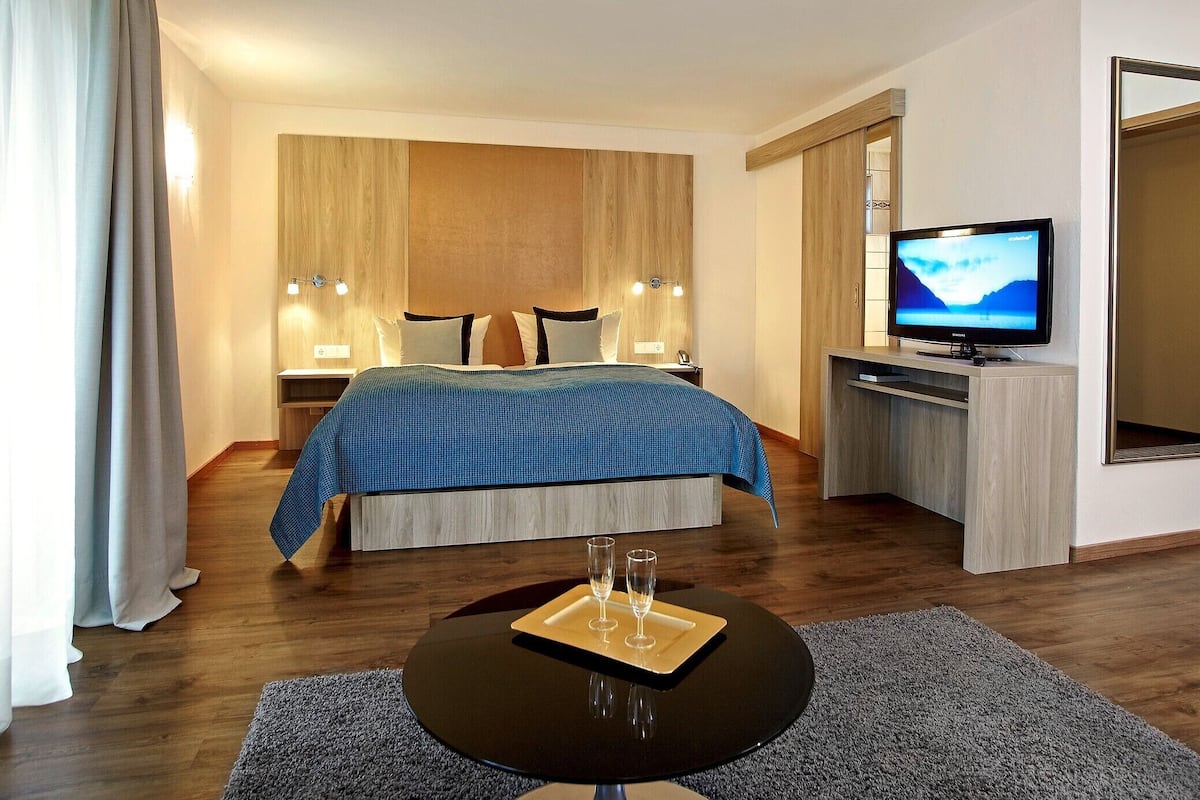 Une chambre d’hôtel avec un lit, des tables de chevet, une télévision et une petite table avec des verres.