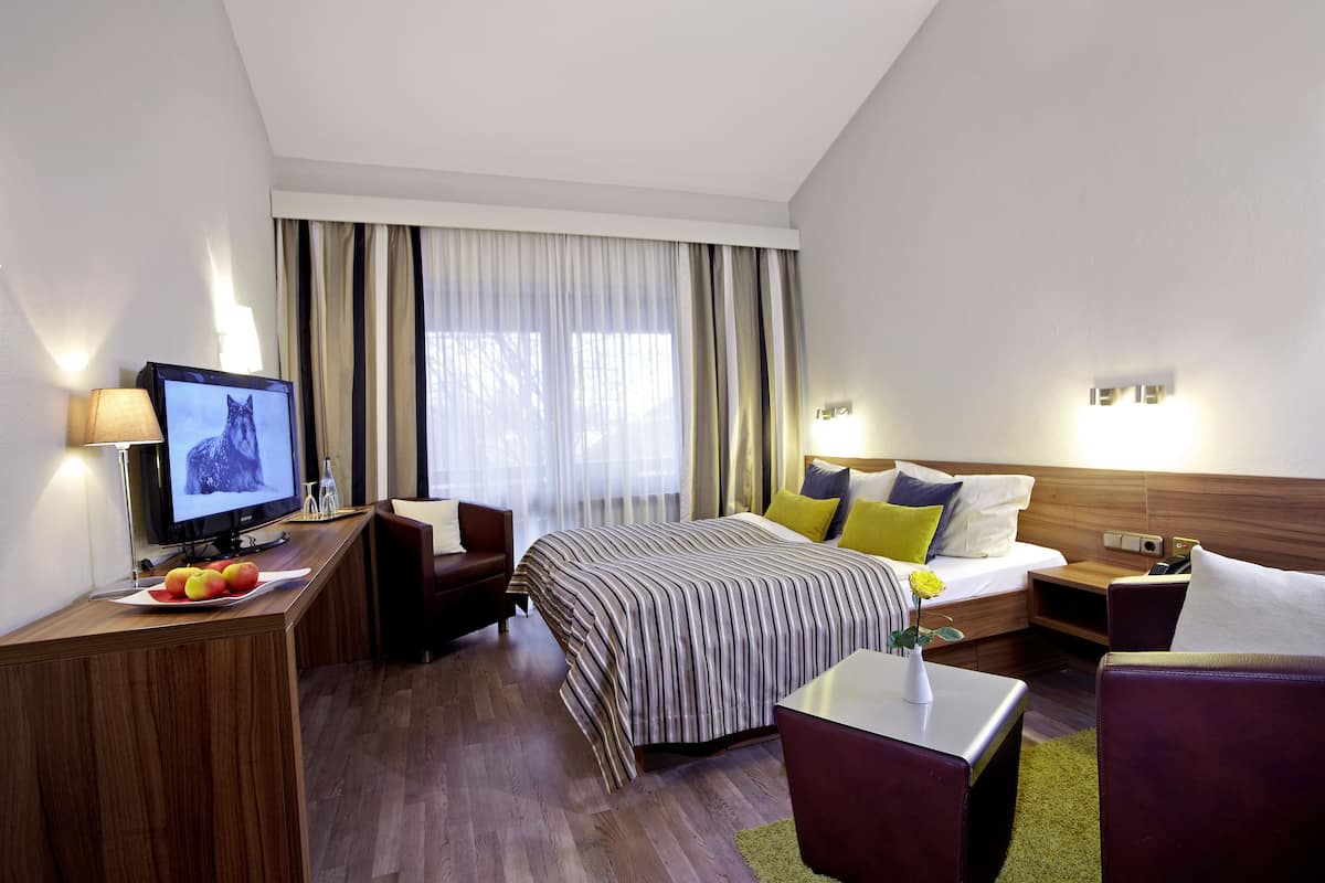 Une chambre d’hôtel moderne équipée d’un lit, d’un bureau avec un ordinateur, d’une télévision et d’un petit coin salon.