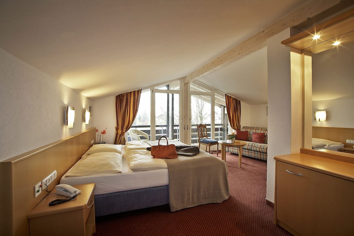 Une chambre d’hôtel comprenant un lit, un bureau avec un téléphone, une chaise, un canapé, un miroir et une fenêtre avec des rideaux.