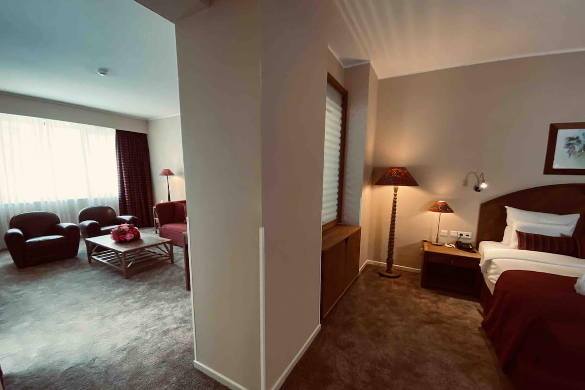 A hotel room with a bed, a nightstand, a lamp, a chair, a sofa, and a coffee table.