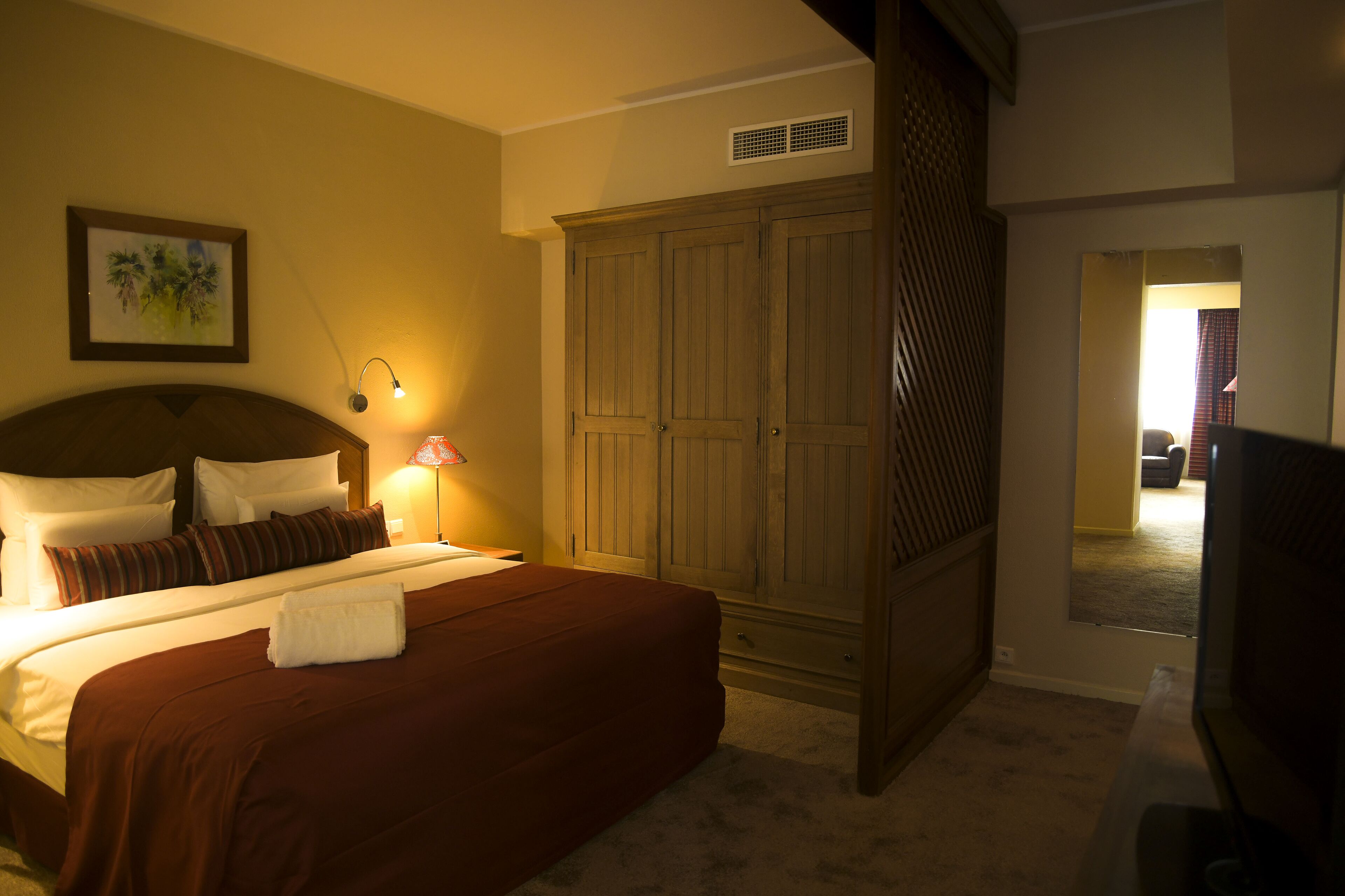 A hotel room with a large bed, a wardrobe, a desk, and a television.