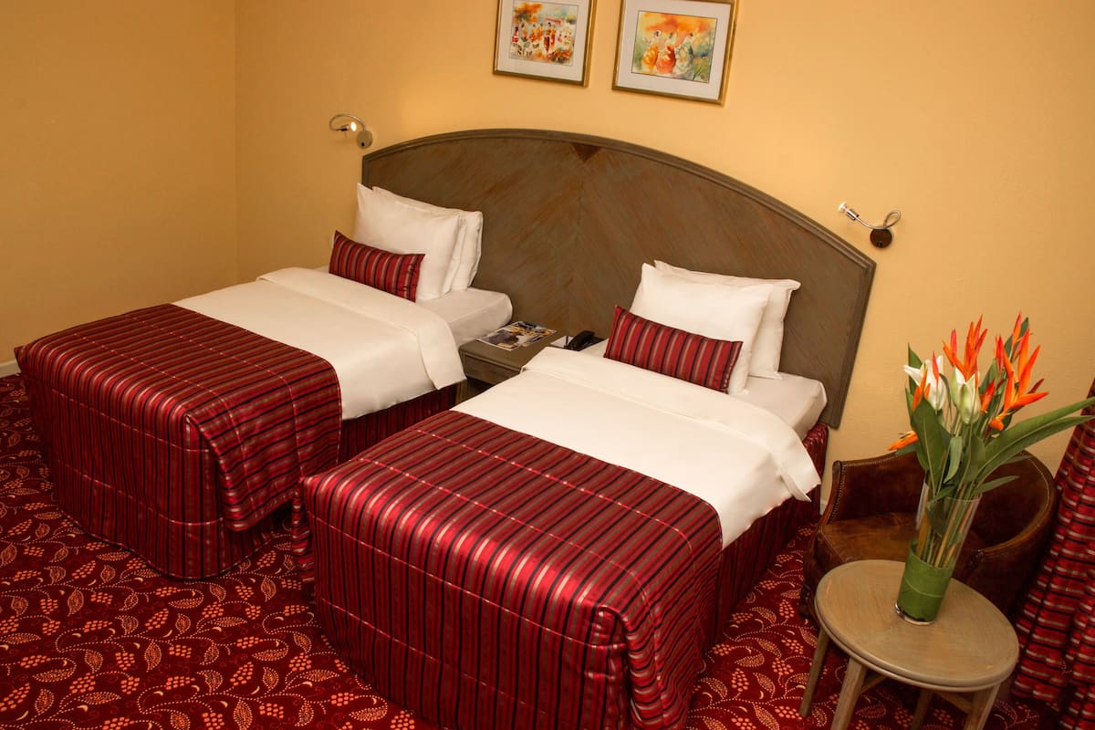A hotel room with two beds, each with a striped red bedspread and white linens. There is a small round table with a vase of flowers.