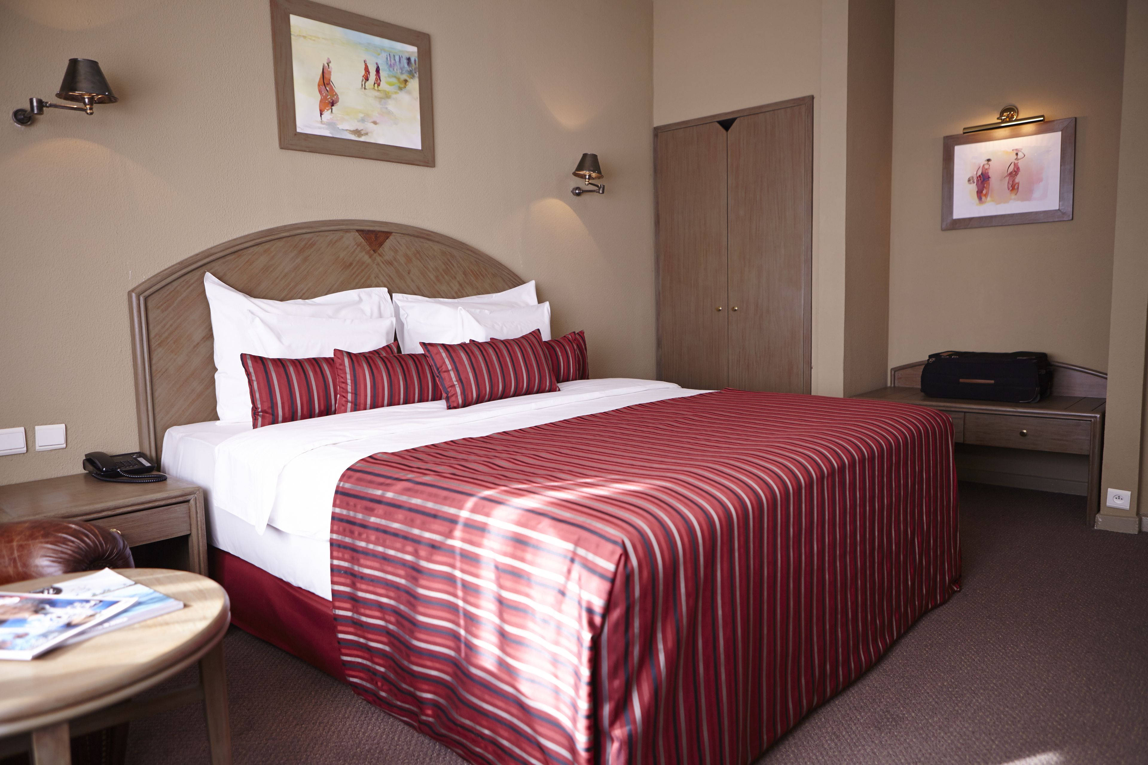 Habitación de hotel con una cama grande, una mesita de noche con lámpara, un atril y una silla. Cuenta con un armario y un escritorio con una silla.