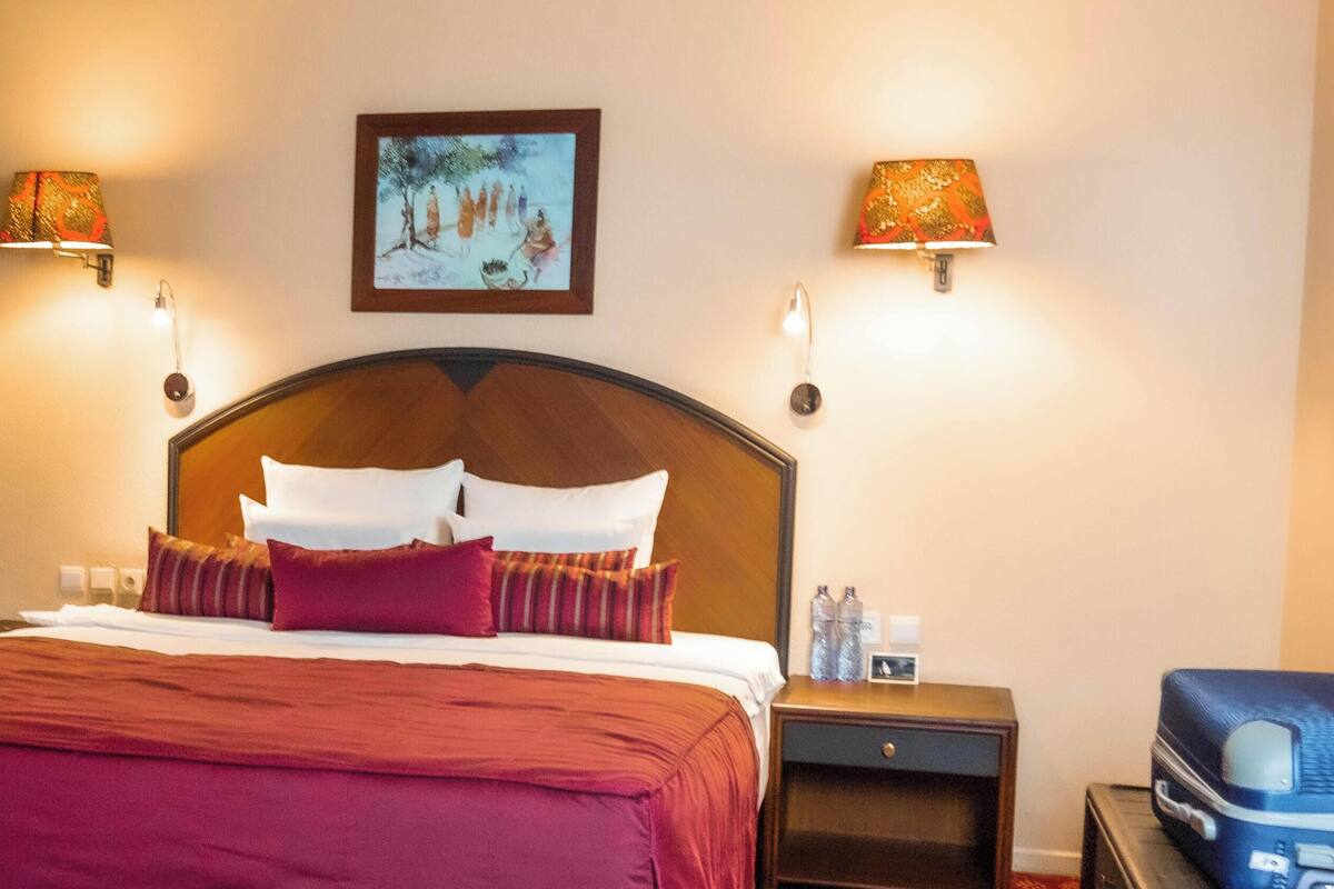 A hotel room with a large bed, two wall-mounted lamps, a nightstand with a lamp, and a suitcase.