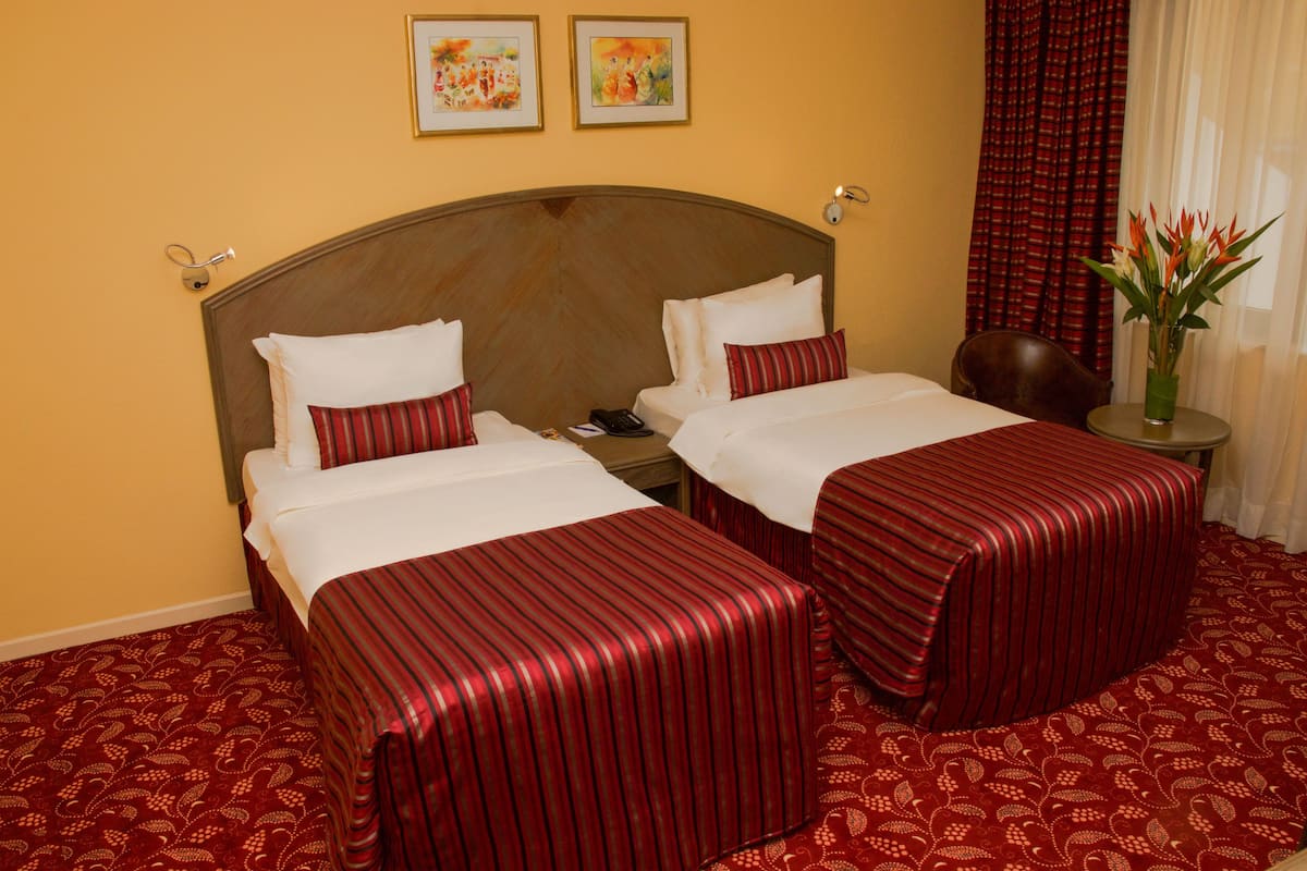 A hotel room with two beds, a wooden headboard, a small table with a vase of flowers, and a chair.