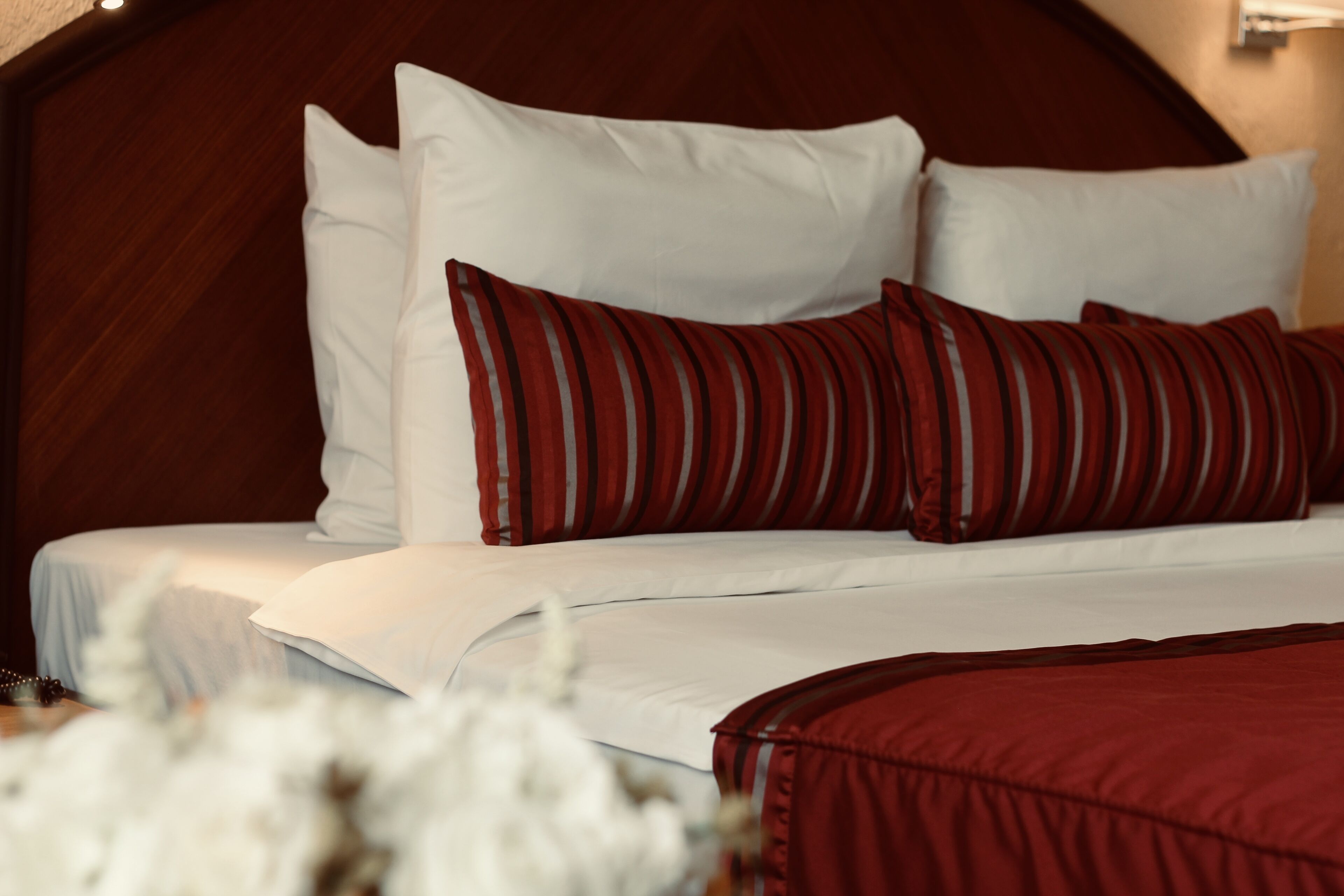 Una cama con almohadas blancas y a rayas, un cabecero de madera y una colcha roja.