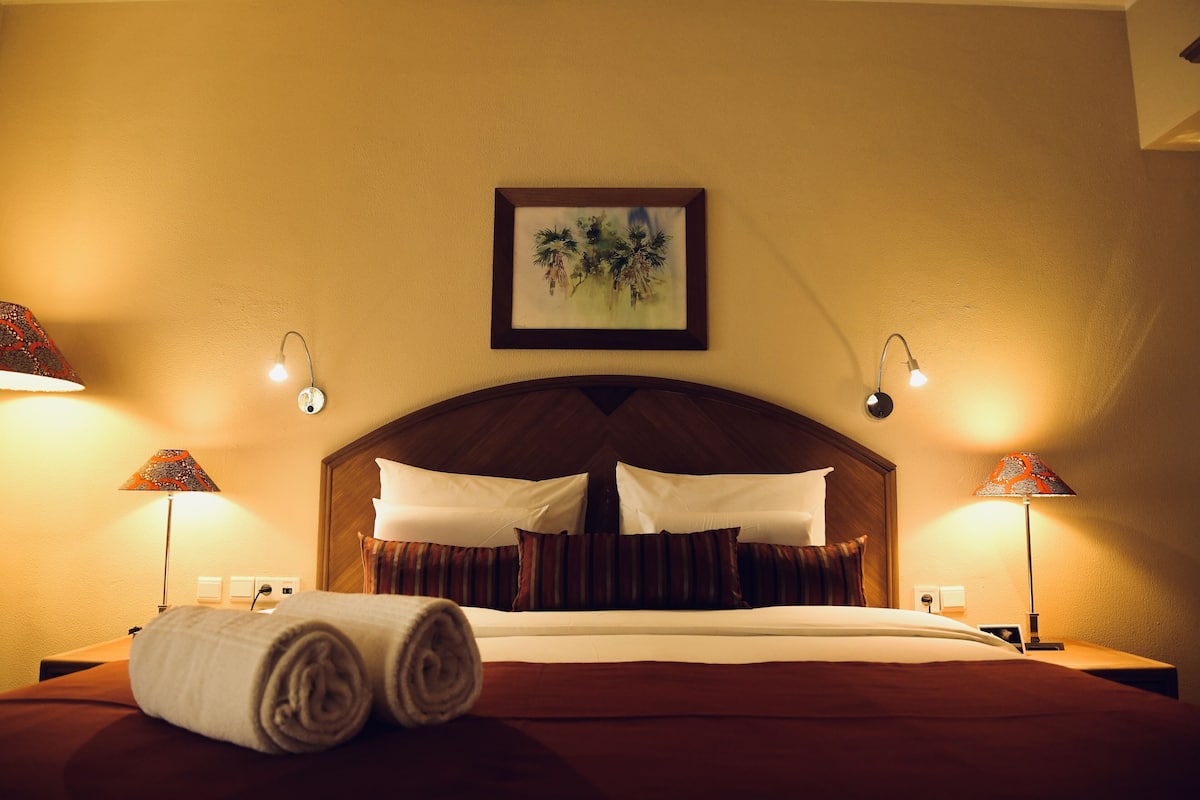 A hotel room with a neatly made bed, two bedside lamps, and a framed artwork on the wall.
