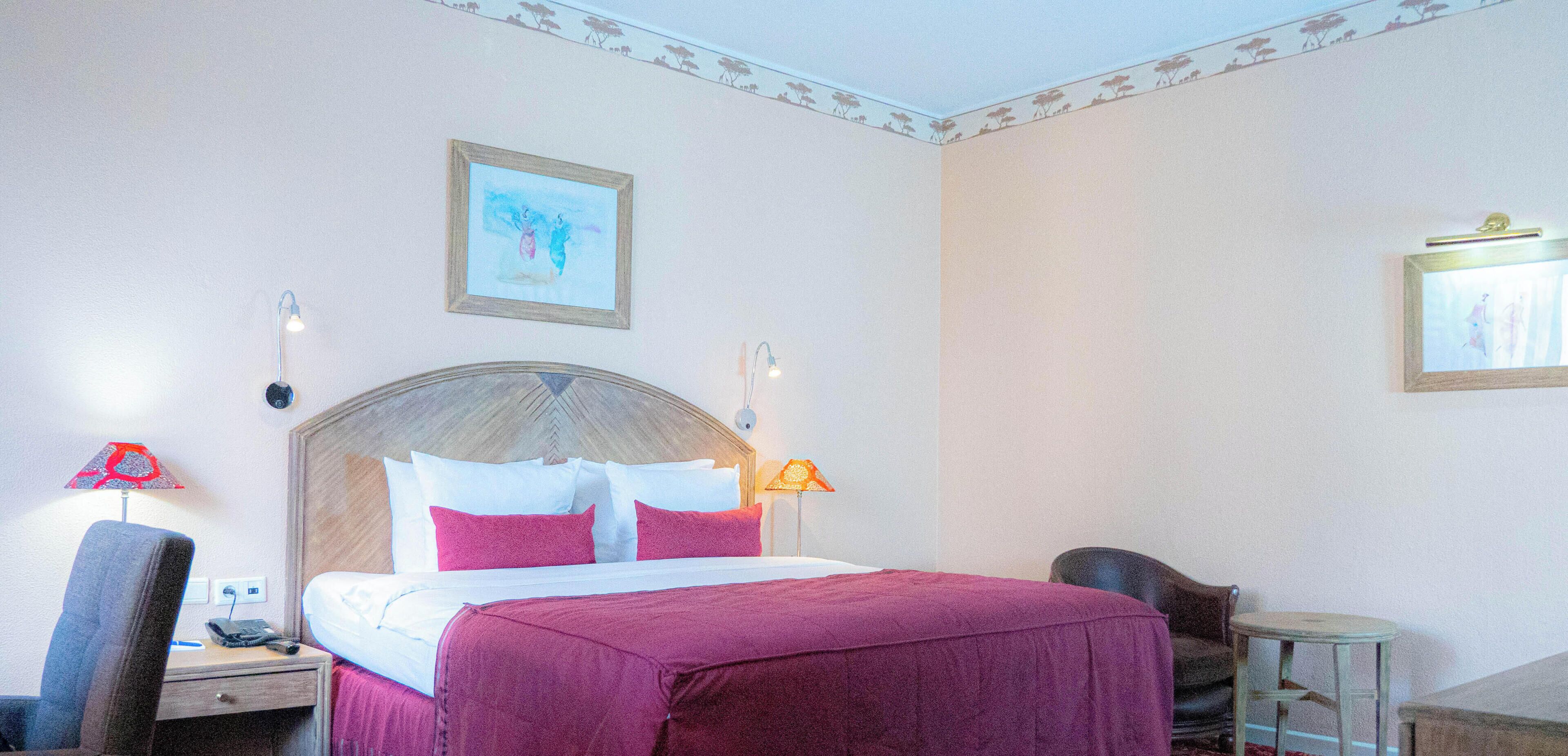 A hotel room with a bed, bedside lamps, a chair, a small table, and two framed pictures on the wall.