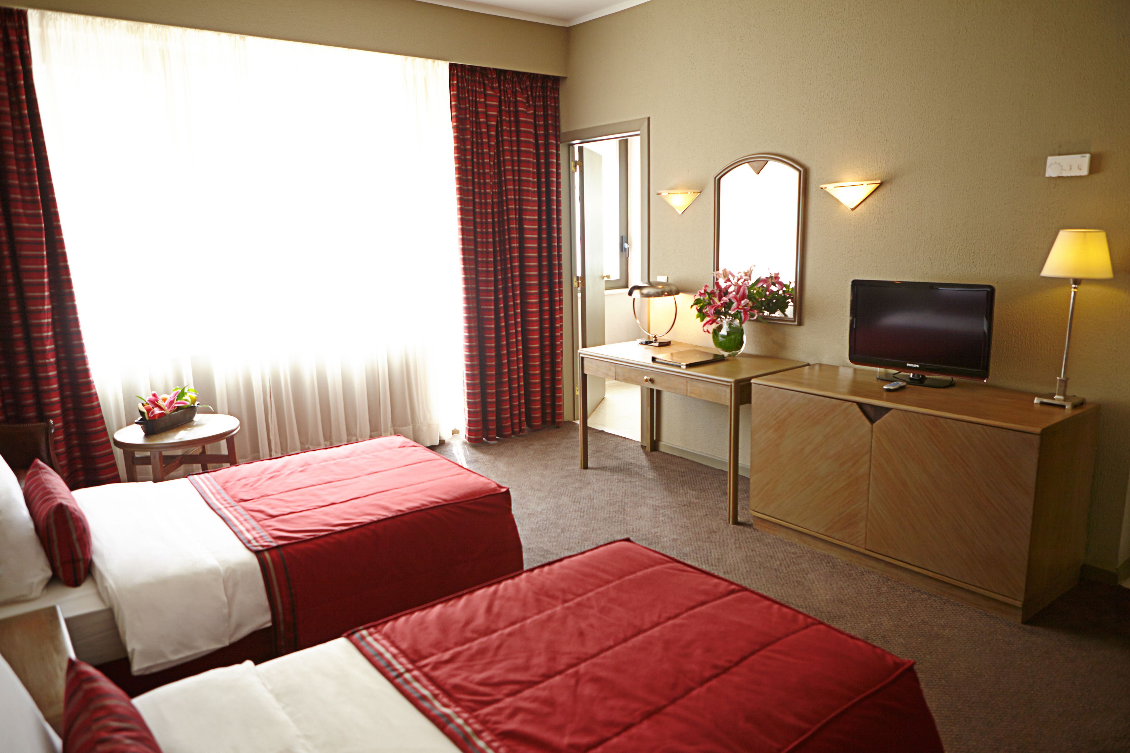 A hotel room with two beds, a desk with a TV, a lamp, and a small table with flowers.