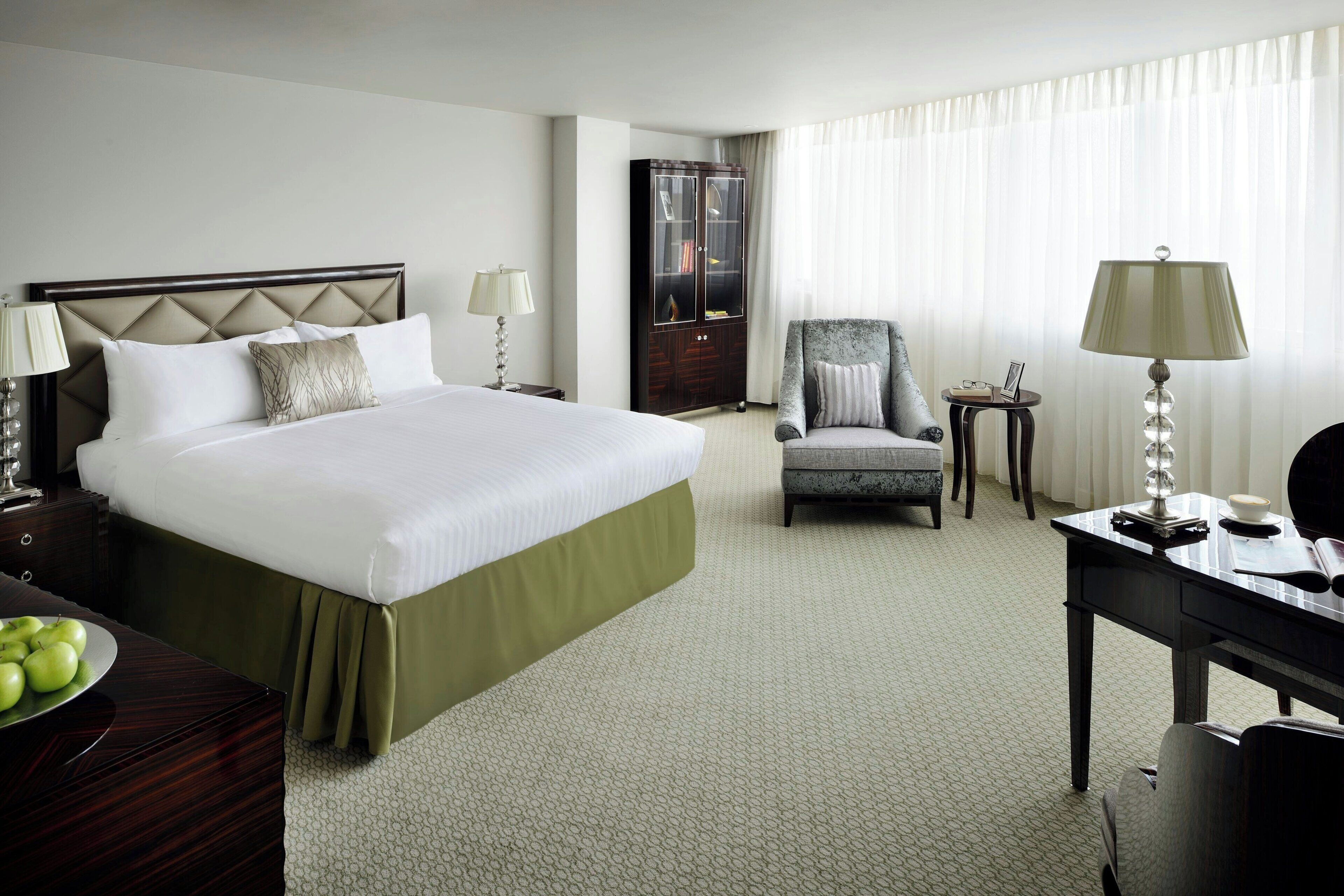 A hotel room with a large bed, a chair, a desk, and a cabinet.