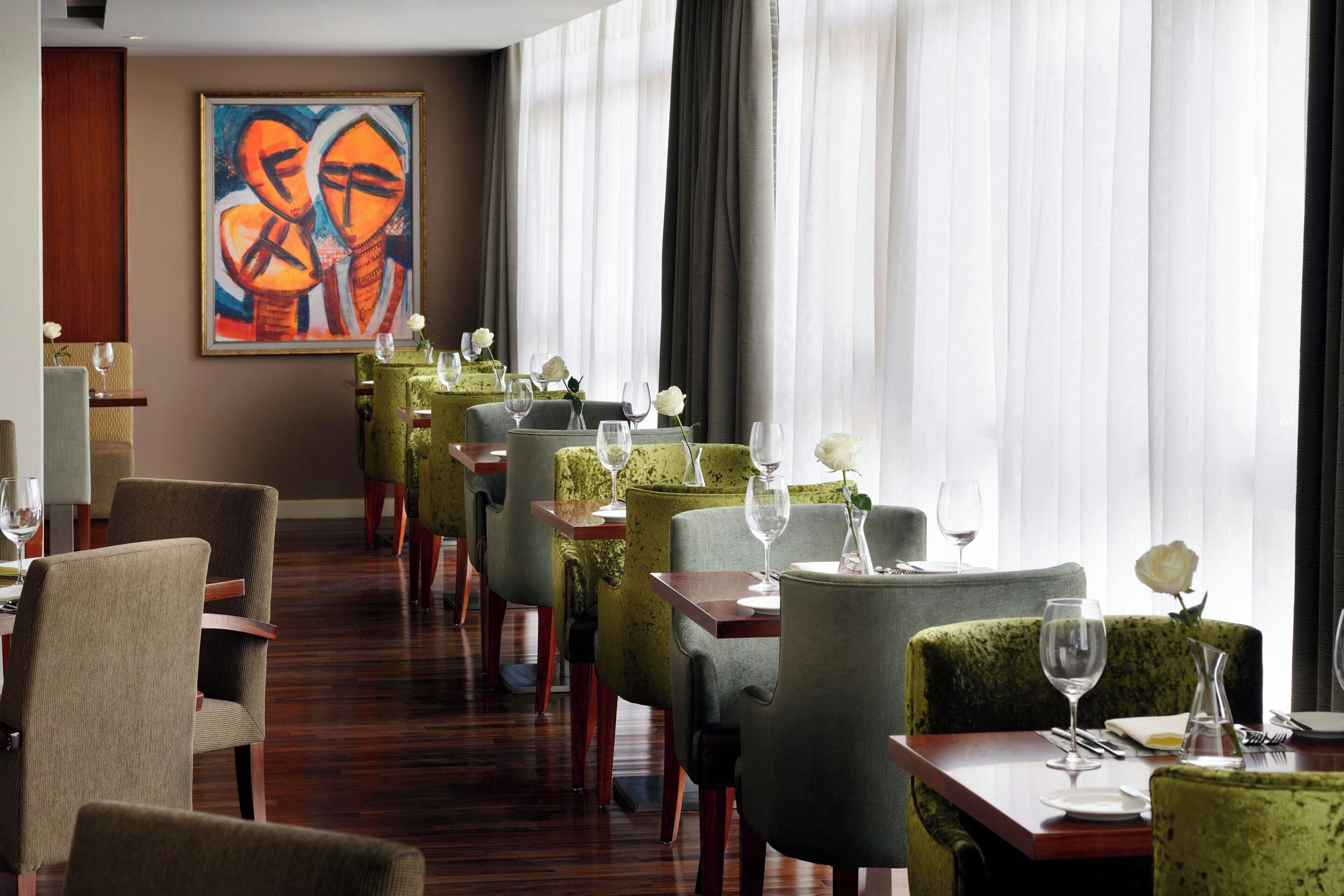 A restaurant with a long table, chairs, and a painting on the wall.