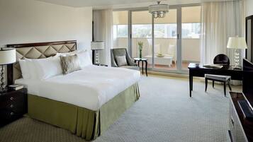 A hotel room with a large bed, a desk, a chair, a lamp, and a view of the city through the window.