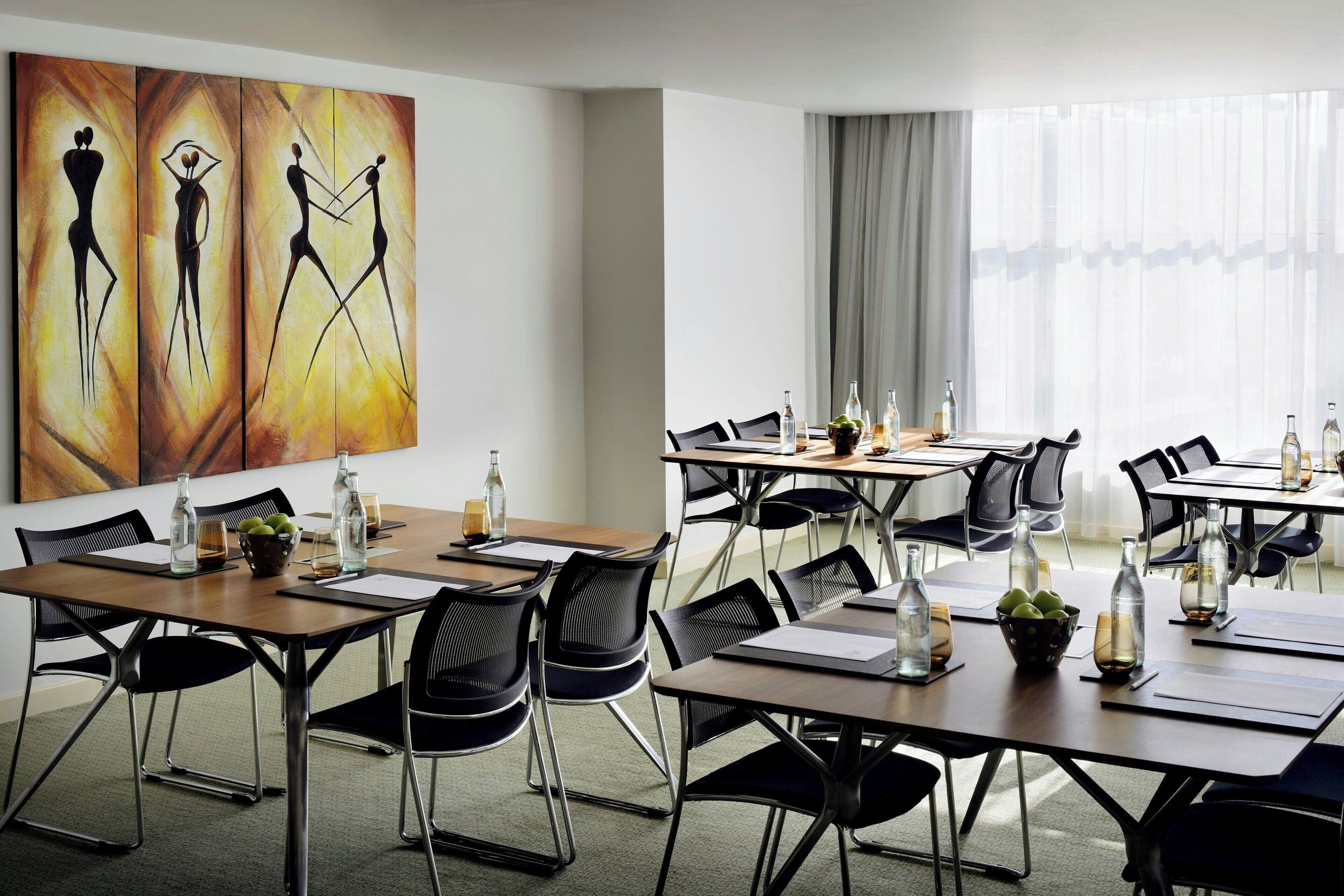 Ein moderner Konferenzraum mit mehreren Tischen, Stühlen und abstrakter Kunst an der Wand.