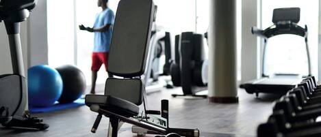 Un gimnasio con equipamiento de ejercicio, una cinta de correr y una persona usando una máquina de fitness.
