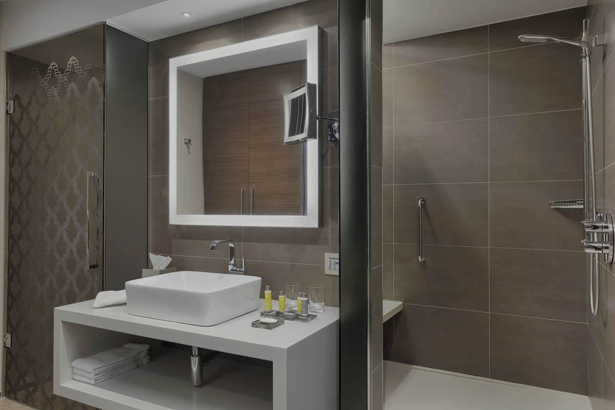 A modern bathroom with a large mirror, a white sink, and a shower area.