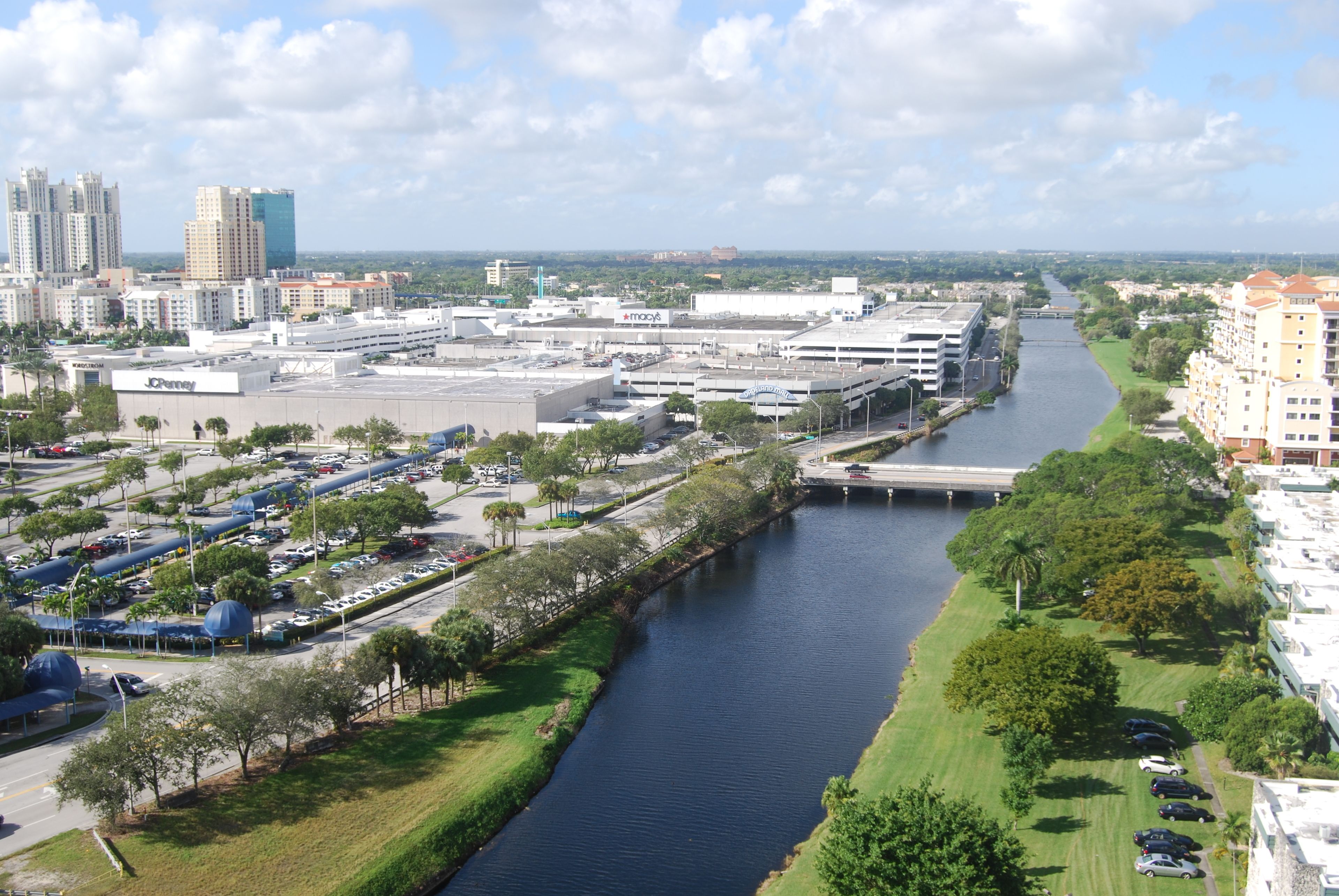 A river running through a city with buildings, a parking lot, and greenery.