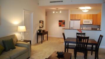 A living room with a sofa, a coffee table, a dining table with chairs, a kitchen area with a microwave, and a framed picture on the wall.