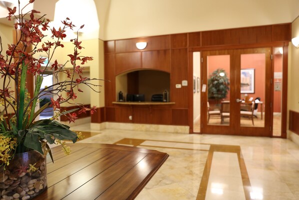 Un hall d’hôtel avec un comptoir d’accueil en bois, une plante en pot et un sol en marbre.