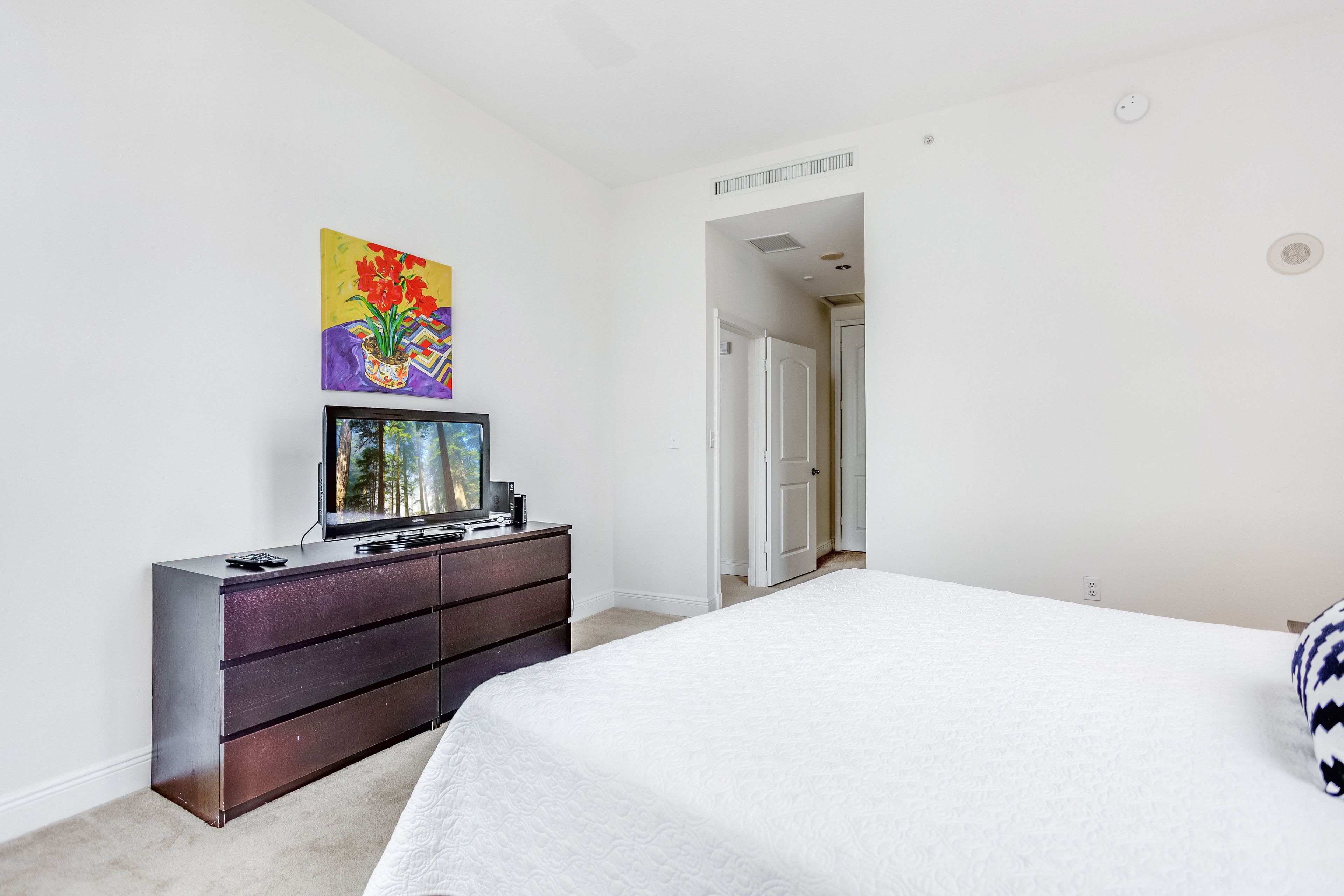 A bedroom with a bed, dresser, TV, and artwork on the wall.
