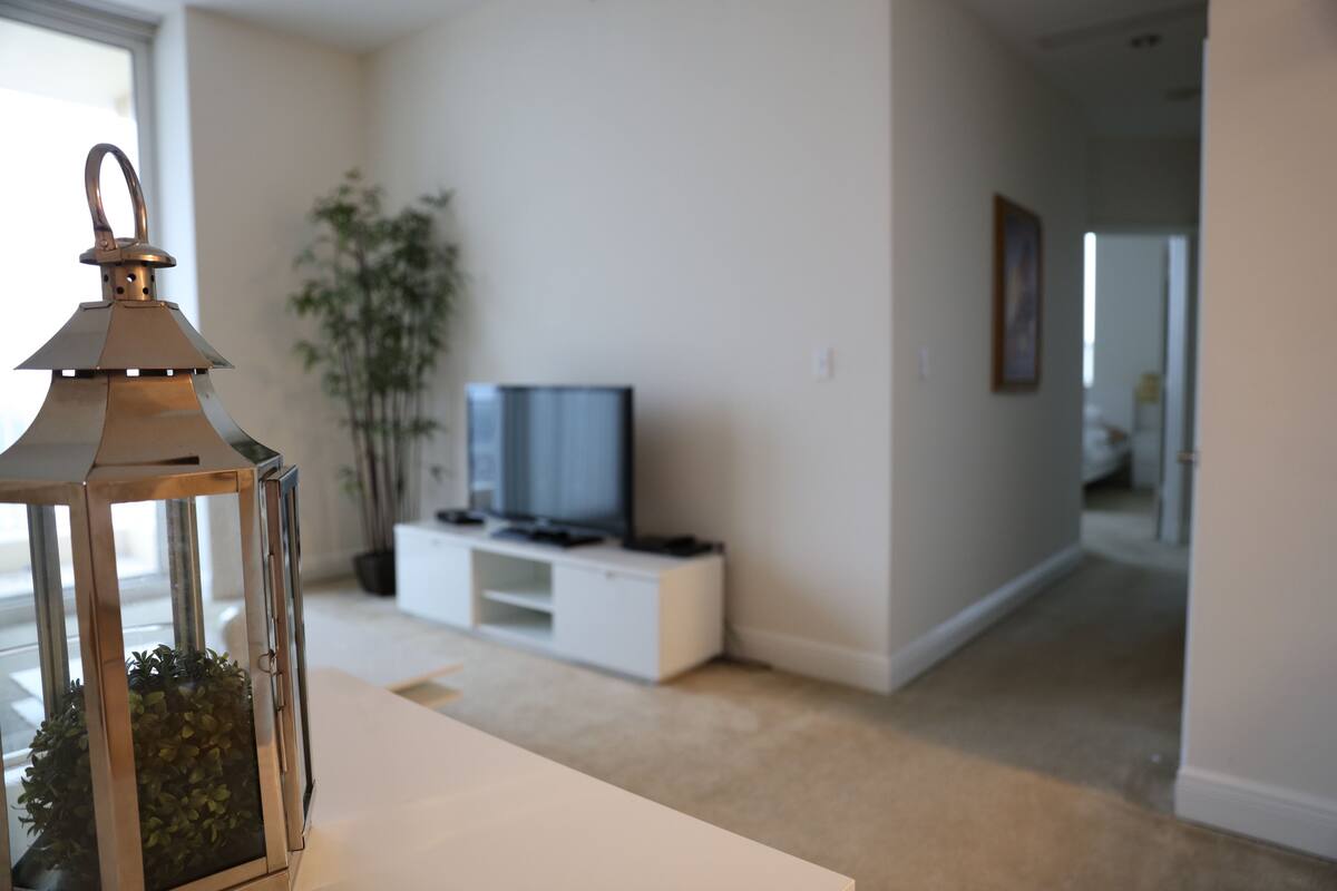 Una sala de estar moderna con un televisor sobre un mueble blanco, una planta y un farol sobre una mesa.