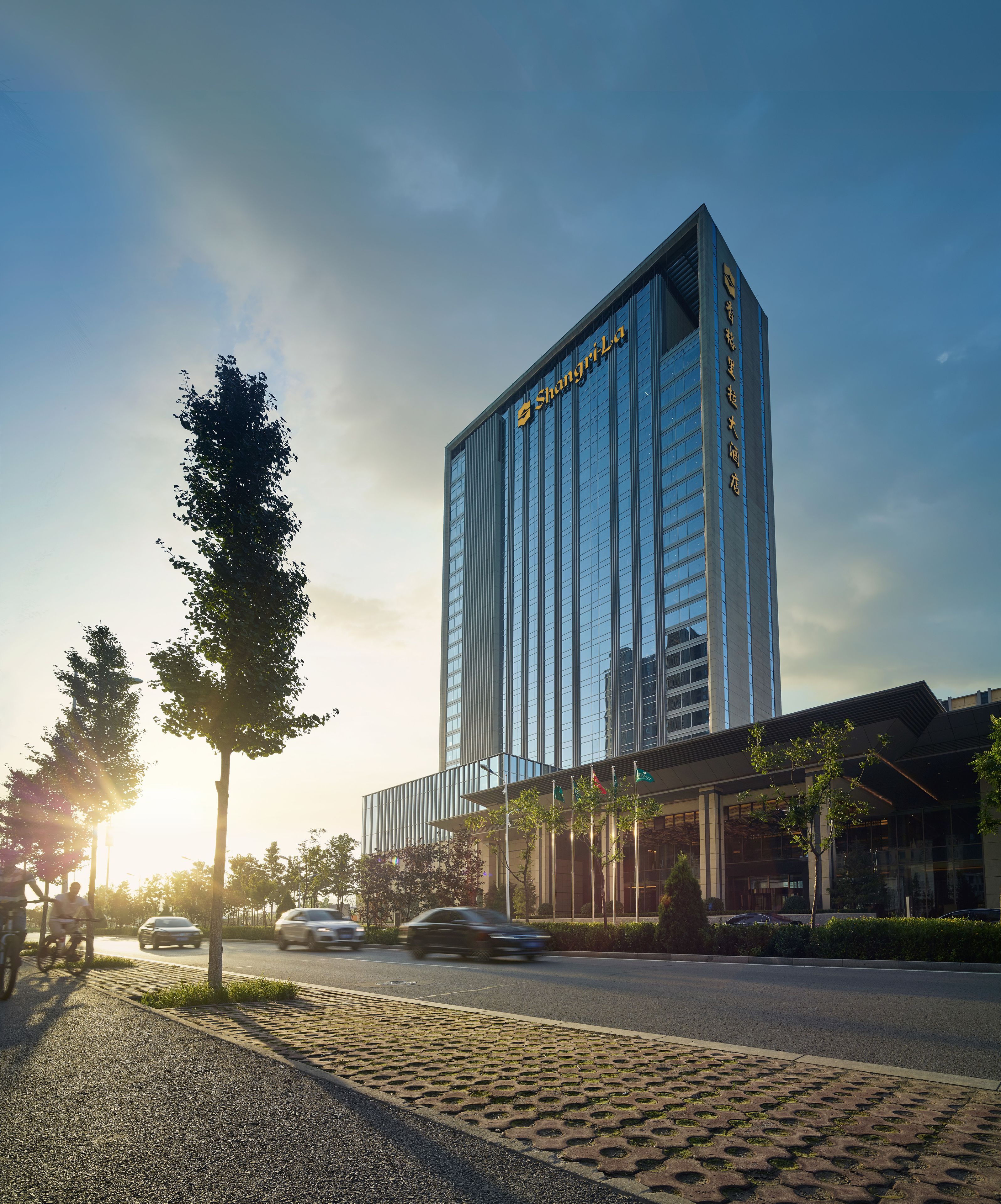 A modern hotel with a prominent glass facade and a vertical sign displaying the name.