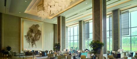 A spacious lobby with a central seating area, large windows, and a modern chandelier.