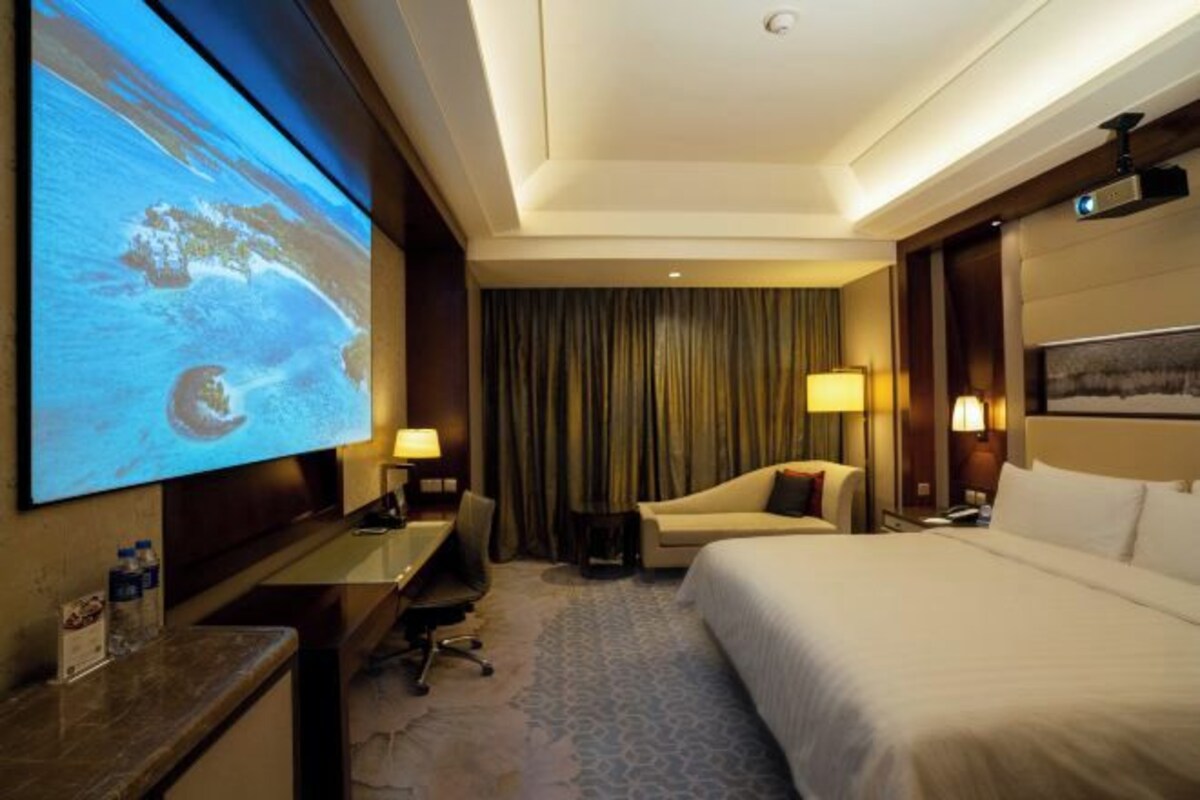 A hotel room with a large bed, a desk with a chair, a television mounted on the wall, and a window with curtains.
