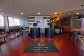 Zona de recepción de un hotel con diseño moderno, que incluye un mostrador de recepción, un área de estar y un gran ventanal con cortinas.