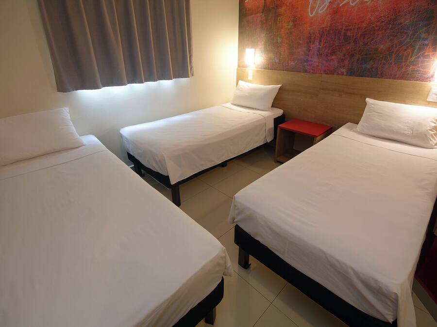 A hotel room with three single beds, a red nightstand, and a large abstract painting on the wall.
