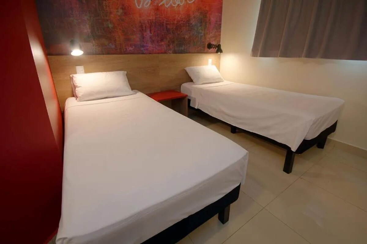 Habitación de hotel con dos camas individuales, cabecero de madera, pared de acento roja y un cuadro abstracto grande.