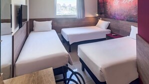 A hotel room with two single beds, a TV, a window with a view of the city, and a motivational wall art.