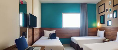 Habitación de hotel con dos camas, un escritorio con una computadora portátil, un televisor y una ventana con cortinas.
