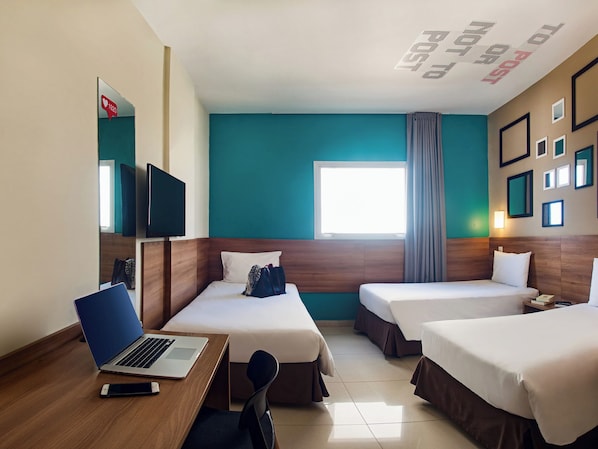 Une chambre d’hôtel avec deux lits, un bureau avec un ordinateur portable, une télévision et une fenêtre avec des rideaux.