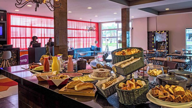Un espace buffet proposant divers plats, un coin salon avec un canapé bleu et une grande fenêtre ornée de rideaux rouges.