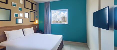 Een hotelkamer met een groot bed, een flatscreen televisie, een raam met uitzicht op de stad en beelde op de muur.