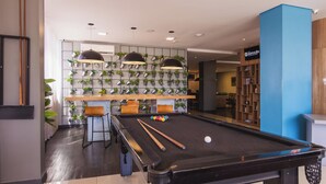 A pool table with pool cues and balls, a wall with potted plants, and a blue pillar.