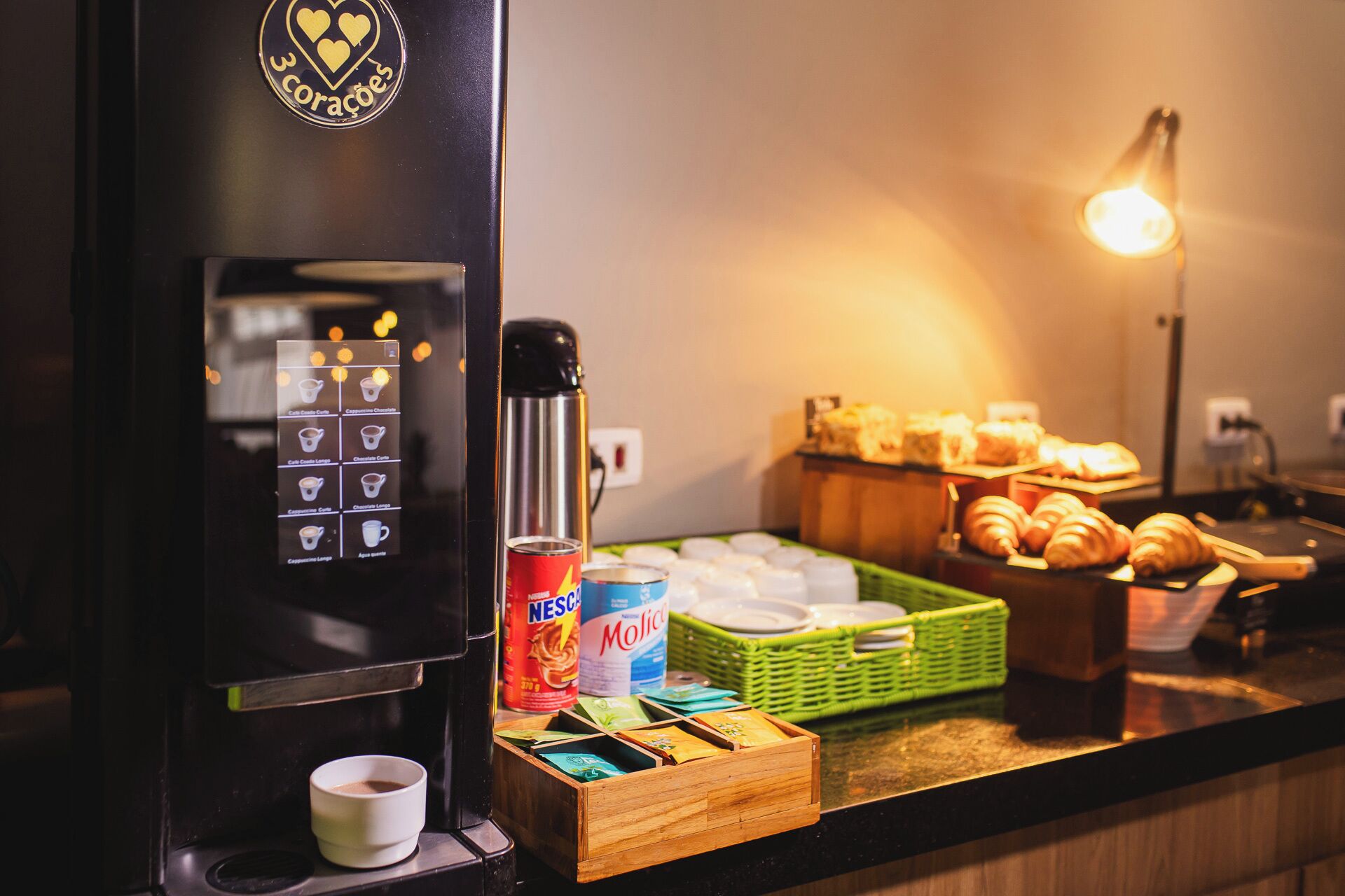 Máquina de café com visor digital, uma térmica, cesta de pastelaria e uma chávena de café.