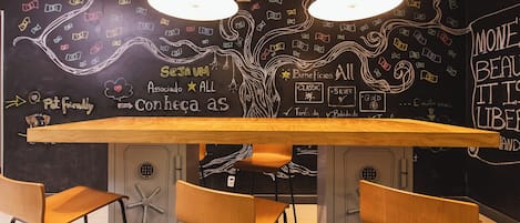 A modern cafe with a wooden table and chairs, a chalkboard wall with doodles and text, and pendant lights.