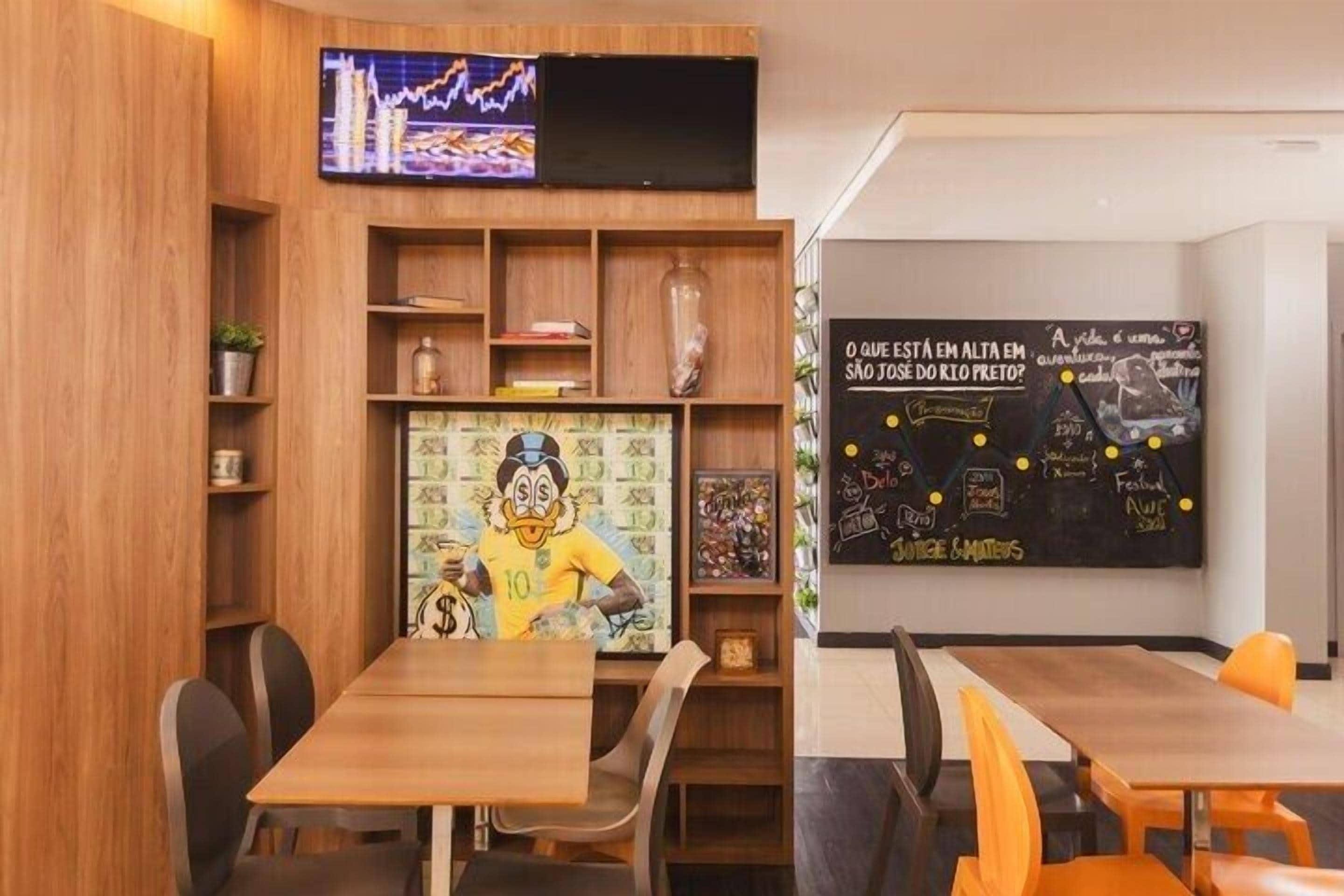 A restaurant with wooden furniture, a TV displaying a graph, and a chalkboard with drawings and text.
