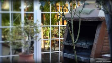 Una parrilla de horno de ladrillo, una planta en maceta y una ventana con diseño de cuadrícula.