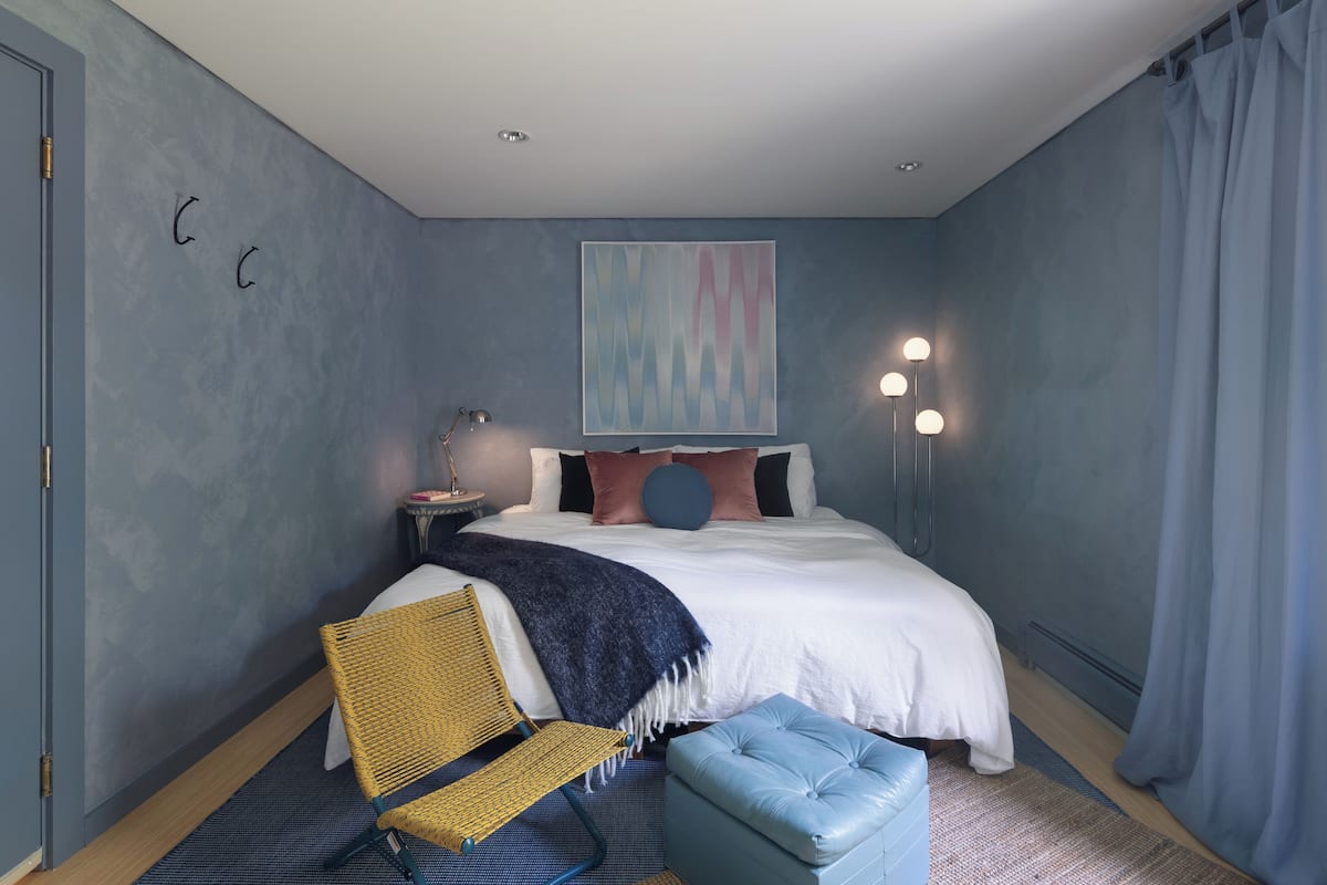 A bedroom with a bed, a chair, a bedside table, and a wall-mounted artwork.