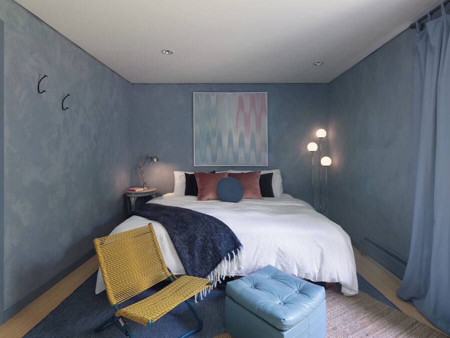 Un dormitorio con cama, una silla, mesita de noche y un cuadro colgado en la pared.