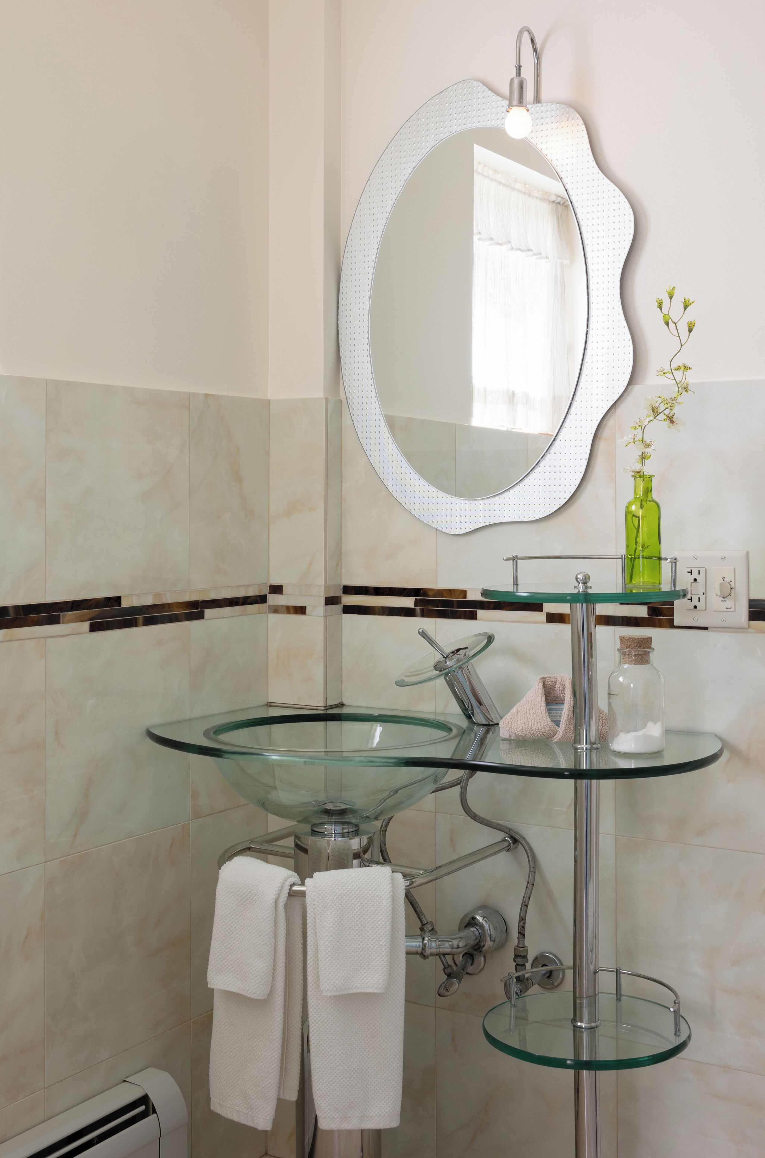 Une salle de bain avec un lavabo en verre, un miroir rond et un porte-serviettes.